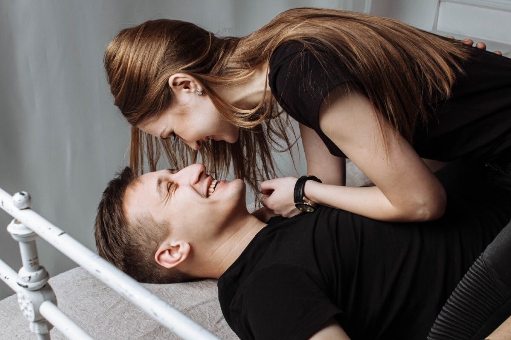 a blonde woman leans over the man trying to trick him into a passionate kiss